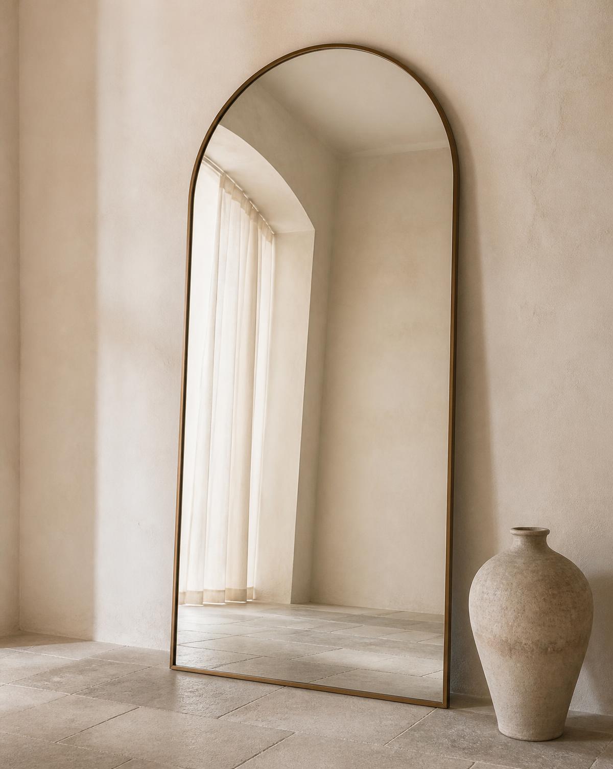 Espejo decorativo en arco con marco de bronce apoyado en muro de estuco
